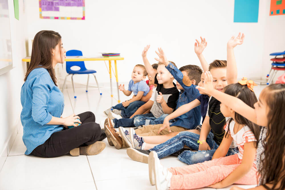 Professora e alunos sentados no chão em sala de aula